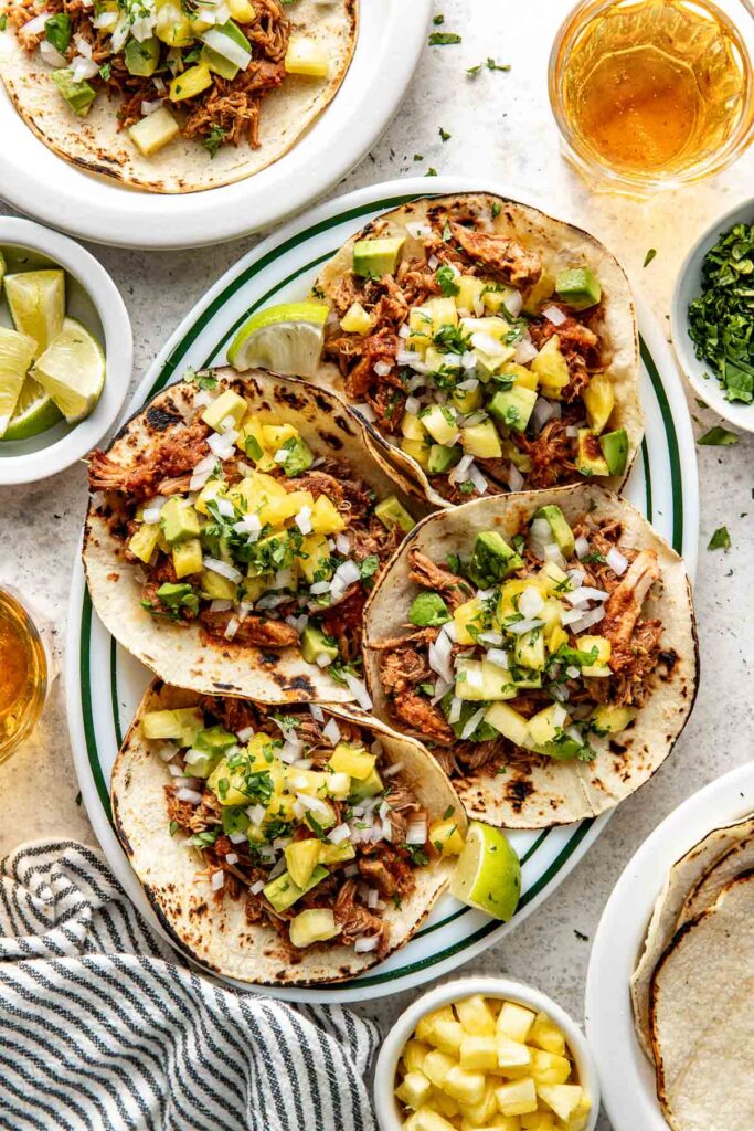 Overhead view of a large plate filled with four Tacos Al Pastor topped with pineapple, onions, and fresh cilantro.